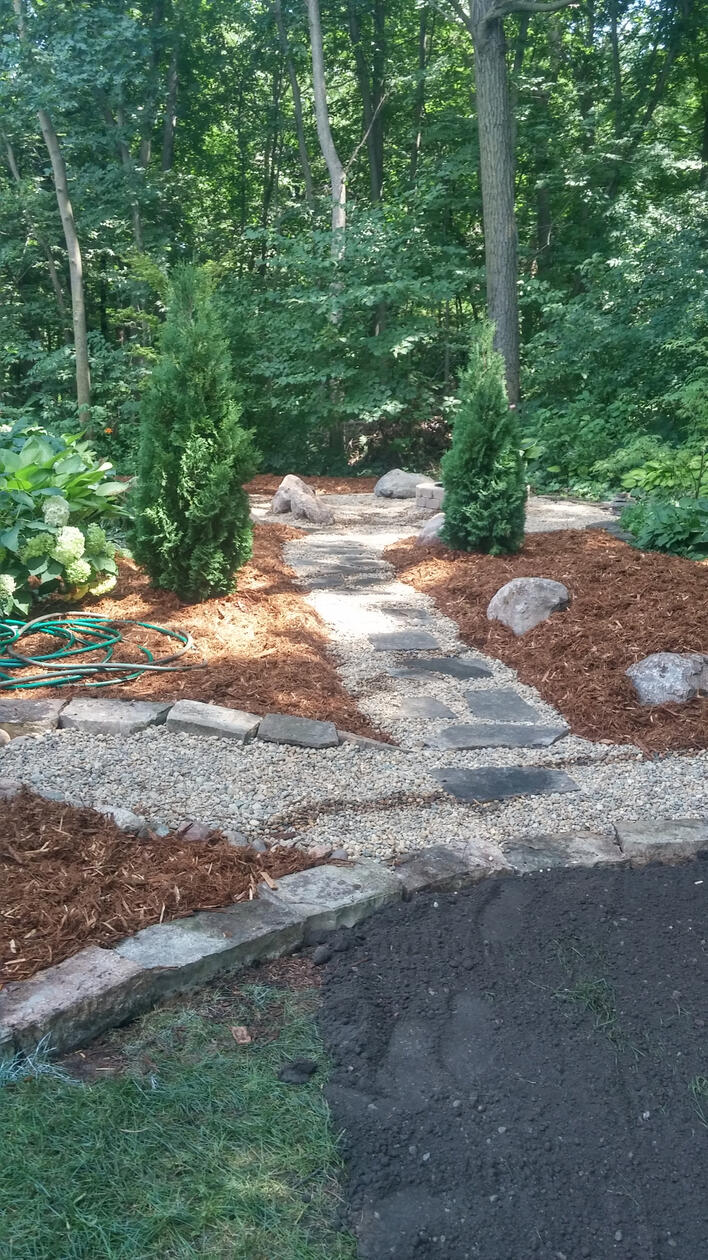 Gravel and flagstone stepper path leading to firepit with boulder seating